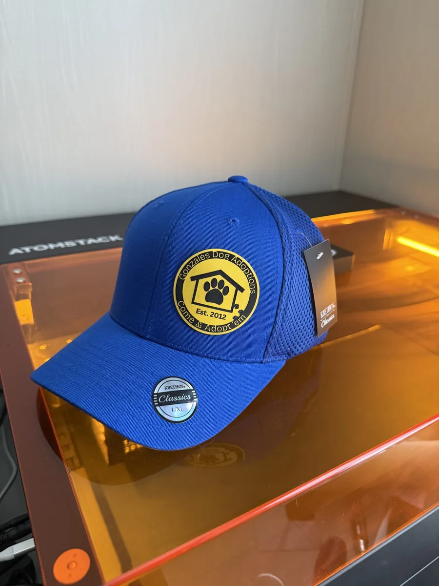 Blue cap with the Gonzales Dog Adoptions logo on a yellow engraved patch