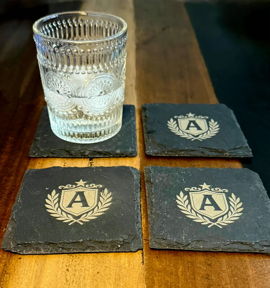 Four dark slate coasters engraved with a custom monogram