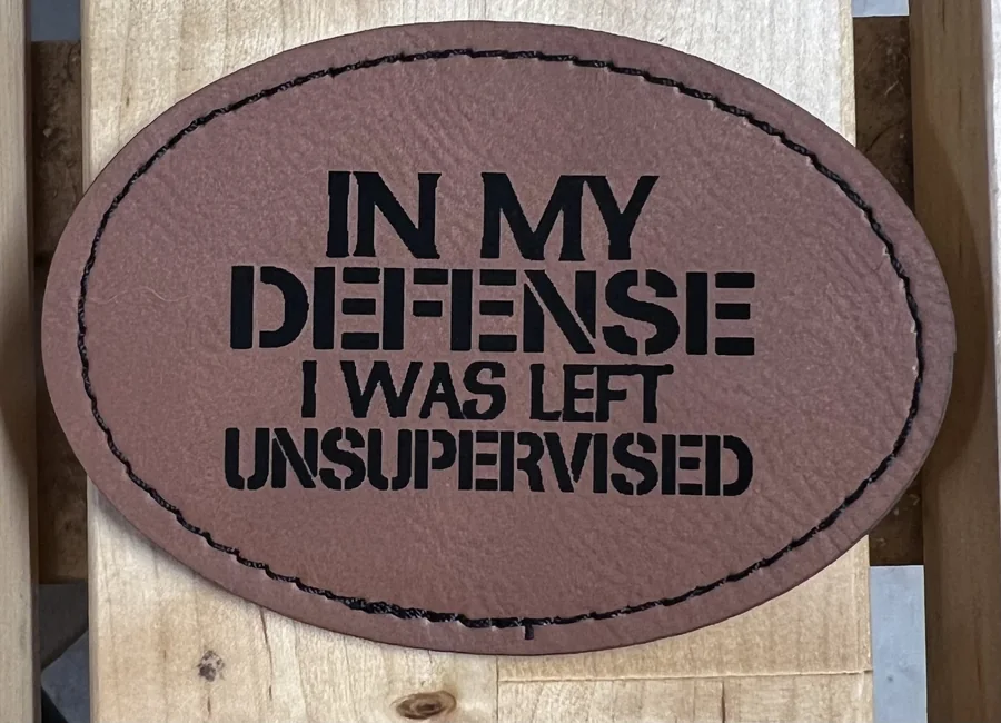 Oval brown leatherette patch with a humorous engraved message
